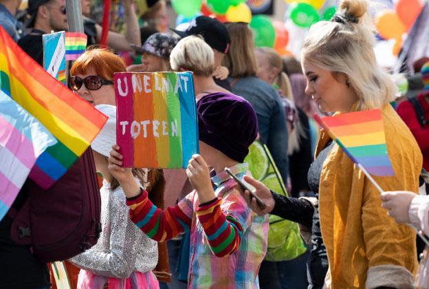 Iloisia ihmisiä Pride-lippujen ja -kylttien kanssa.